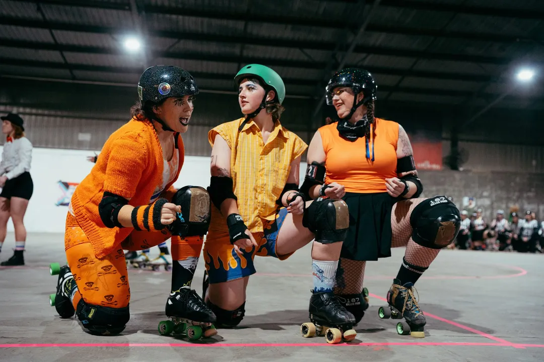 Three skaters in orange crouch at the jam line